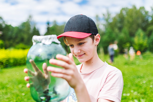 Boy watching butterflies in glass jar. Budget summer vacation at country house