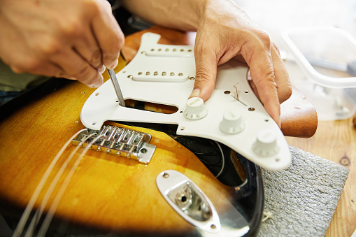 Close-up of the hands of a luthier filing an electric guitar in the workshop.