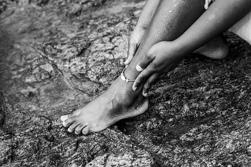 Black and white portrait of woman sitting on beach rock splashing her feet with water. Rio Vermelho Beach, Salvador, Brazil.