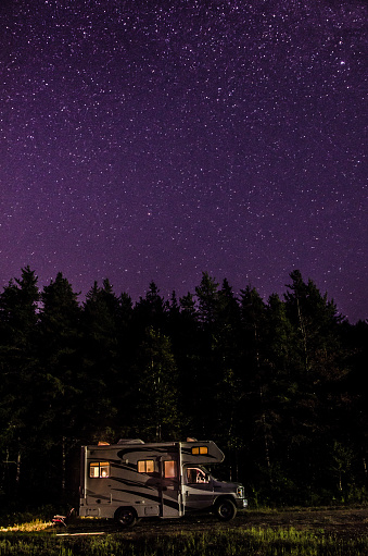 Motor home and night sky with full of stars at blue hour during summer night with woman reading in the motor home