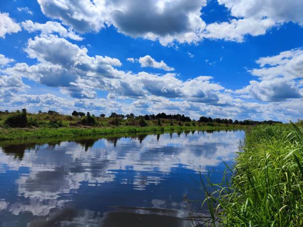 istock Tranquil landscape featuring a river surrounded by lush green grass and trees, and a cloudy sky 1628157398