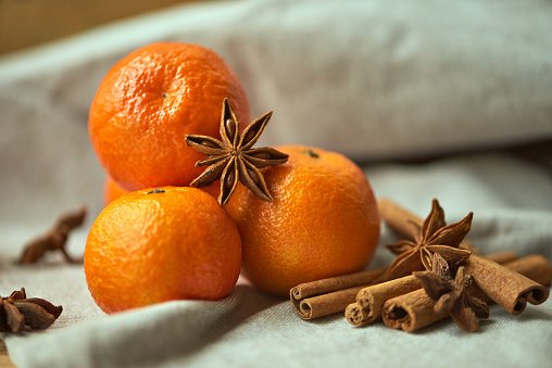 A bunch of ripe tangerines along with cinnamon sticks and star anise on a linen tablecloth. Ingredients for preparing cozy winter hot beverages.