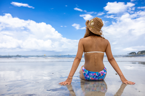 Rear view of tanned woman in bikini sitting in summer beach