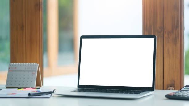 istock Laptop computer with empty display and cup of coffee on white table in bright office interior. 1628280374