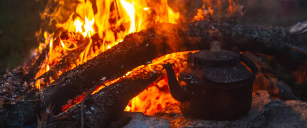 istock Boiling of tea in kettle on bonfire with large firewood. Tea drinking in open air. Active outdoor recreation. Camping in dusk. Romantic warm atmosphere in twilight on nature. Active rest. 1628285156