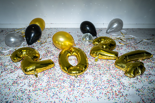 2024 gold foil balloons and colored round balloons abandoned on a floor with lots of confetti