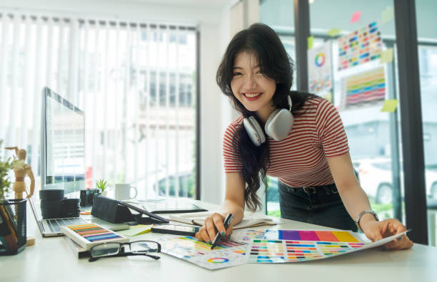 Smiling female creative designer sitting in modern workplace and working with laptop computer.