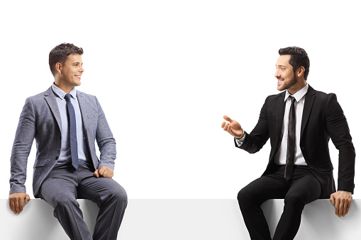 Businessmen sitting on a blank panel and having a conversation isolated on white background