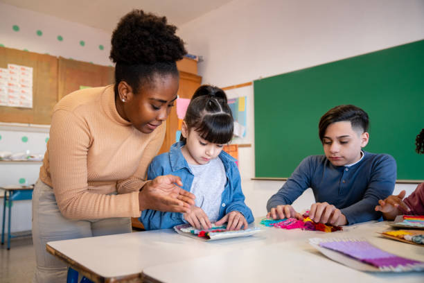 istock African American teacher checking her students work during arts and crafts class at school 1628348799