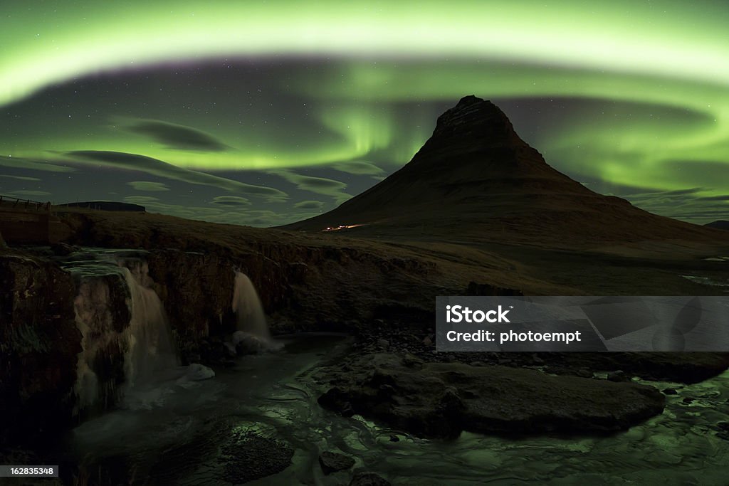 Northern lights over  Kirkjufell mountain, Grundarfjordur, Snaef Aerial view of  double cascade waterfall, Kirkjufellsfoss, and pointed mountain of Kirkjufell, at Grundarfjordur in winter, with  green curving bands of Northern Lights and lenticular clouds in a starry sky, Snaefellnes, Iceland Aurora Borealis Stock Photo