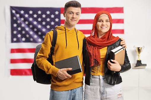 Young male and female student with a hijab holding books in front of an american flag