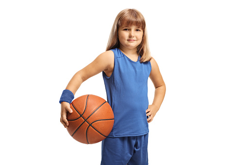 Girl in a blue sports jersey holding a basketball and smiling at camera isolated on white background