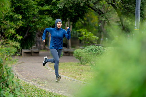 Asian cute muslim woman wearing sportswear and a blue hijab Exercising and running outdoors at the park in the morning. with a fresh feeling.