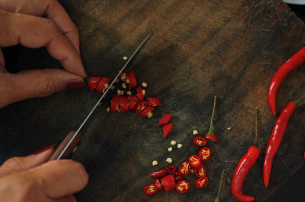 Cropped view hand of woman slices the red chili pepper on the wooden board stock photo