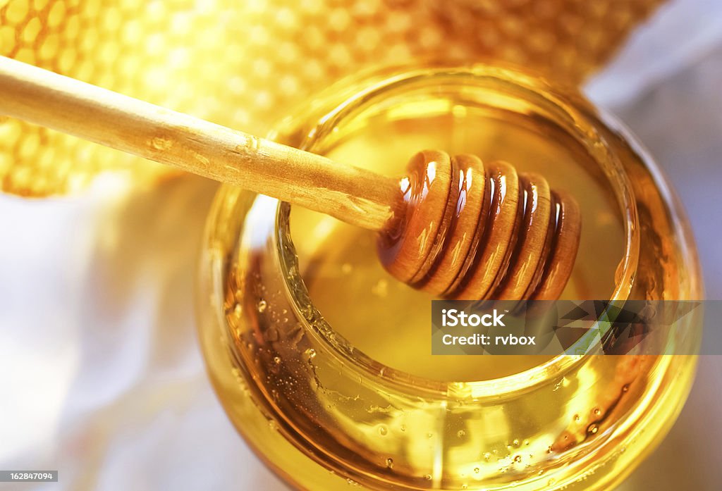 Honey in a glass jar next to honeycombs Honey dipper on the bee honeycomb background. Honey tidbit in glass jar and honeycombs wax. Honey Stock Photo