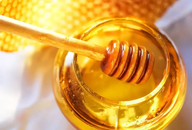 Photo of Honey in a glass jar next to honeycombs