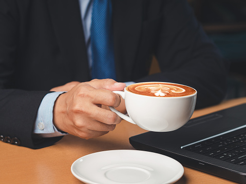 Businessman hand holding a cup of coffee sitting working at the office. Close-up photo. Beverage and relaxation concept