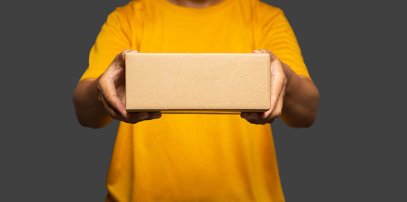 Man in a yellow casual holding a cardboard box while standing on a gray background. Mockup. Space for text. Close-up photo
