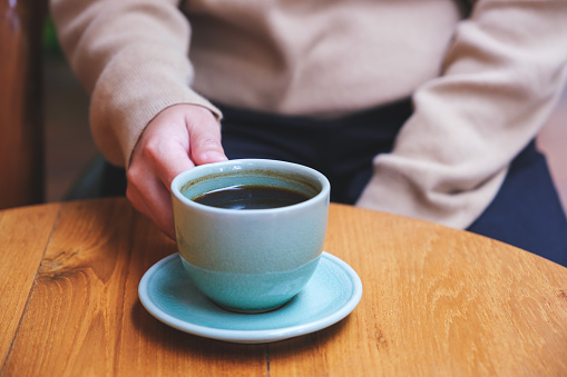 Closeup image of a woman holding a cup of hot coffee on wooden table