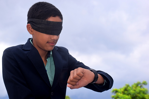 13 year old child with blindfold watching time on clock, Indecision and uncertainty conceptual, cloudy background