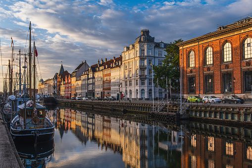 Beautiful sunrise over canal in Copenhagen, Denmark; colorful buildings, sky and boats reflect in calm water