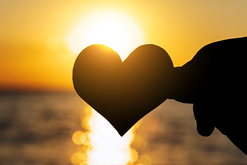 Toned Photo of Heart Shape Silhouette in the Hand on the Sunset on the Sea Background