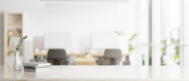 A white tabletop for displaying your product over a blurred bright office room in the background.