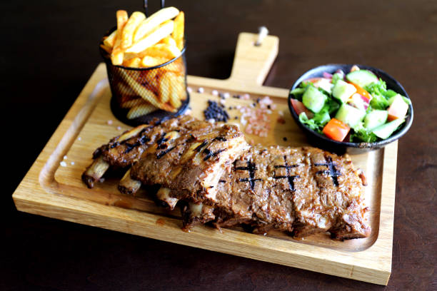 Grilled ribs on wooden background with fries and salad stock photo