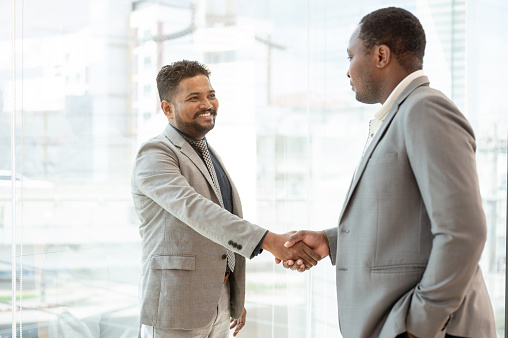 A professional Indian-Asian businessman shakes hands with an African American business partner after a meeting. Greeting, welcome, congratulations, successful business dealing