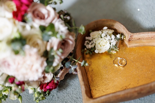 Close-up shot of wedding rings in heart shaped jewelry box with bouquet of roses