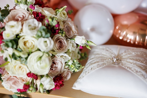 Close-up shot of wedding rings on a silk pillow with bouquet of roses and balloons