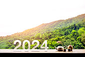 Happy ne year 2024 concept with letter numbers and Asian style hot tea set on wooden table on green mountain view with sunrise in the morning at Chiang Mai, the famous province north of Thailand.