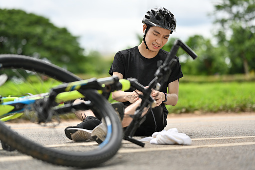 Male cyclist having an accident, falling down from bicycle and injured his knee. Bicycle accident.