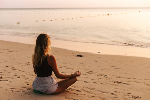 istock Woman meditating on the beach at sunset 1628834457