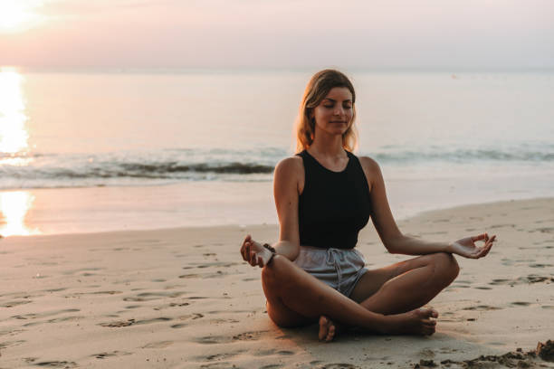 istock Woman meditating on the beach at sunset 1628836091