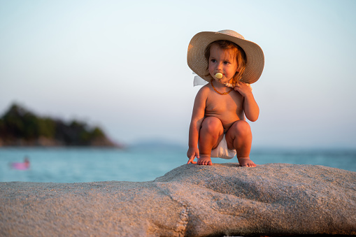 Cute baby girl whit sun hat standing on the rock at the beach