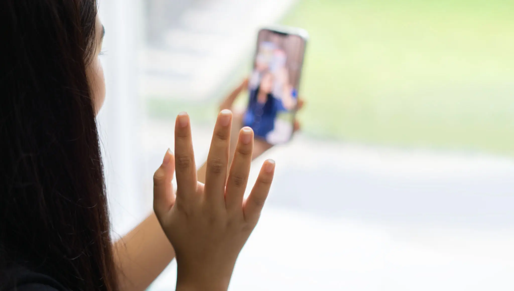 ack view of Asian girl waving hand using smartphone app enjoying online virtual chat video call with friends
