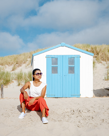 Asian women visiting the beach of Texel with on the background the white blue house on the beach of Texel Netherlands, a beach hut on the Dutch Island of Texel during summer