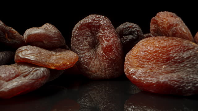 A handful of dried apricots on a black glass table, the camera slowly moves away. macro slide.