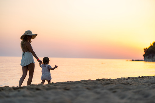 Single mother enjoying with her small girl during summer day on the beach at sunset