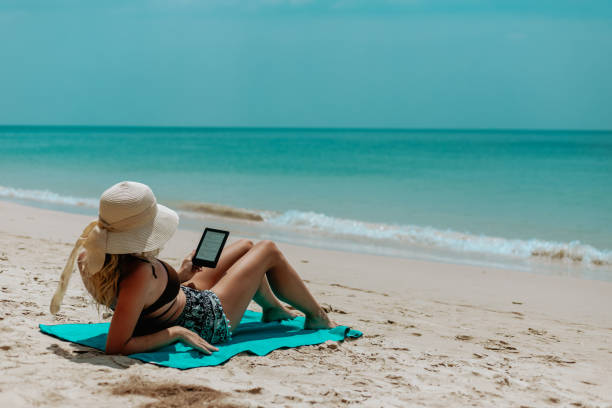 istock Woman with an e-reader on vacation at the beach reading a book 1628902182