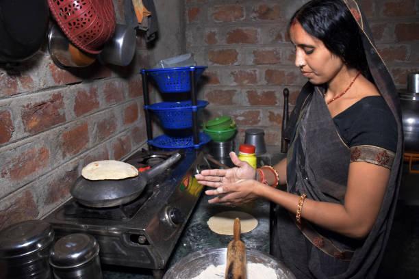 istock An Indian rural housewife while cooking Bread(roti) in an earthen pot using LPG gas, kitchen concept, cook house, brick wall background 1628904919