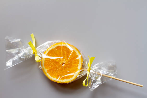 istock Orange slice on stick wrapped in foil, fruit lollipop, healthy substitute for sweets, creative concept 1628914885