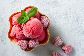 Scoops of cold delicious refreshing raspberry ice cream decorated with frozen raspberries and green mint leaf, served in waffle bowl