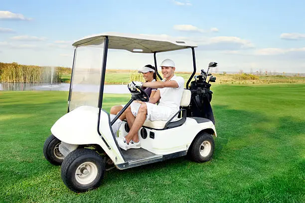 Smiling and happy couple driving a golf-cart with clubs on the back