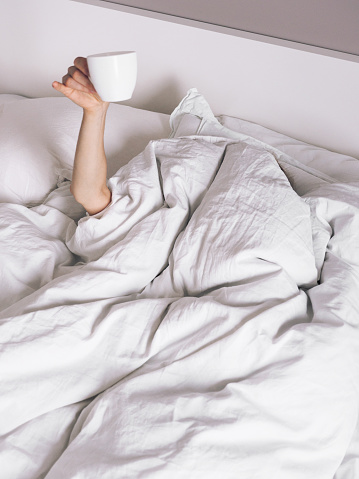 female hand with coffee cup sticking out from the blanket