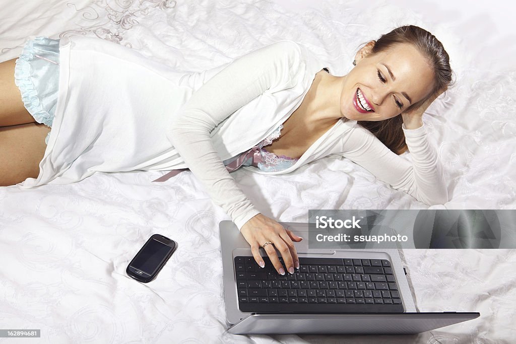 Femme heureuse sur le lit avec ordinateur portable - Photo de Adulte libre de droits