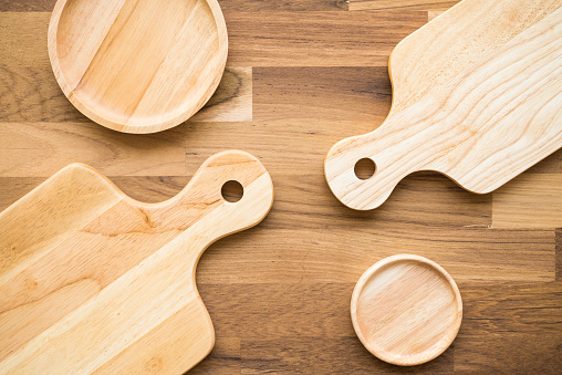 Top view of unused new brown handmade wooden kitchen utensil, dish plate, cutting board and saucer on wooden table background. Kitchen utensil, food concept.