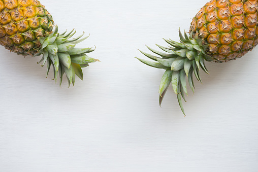 Flat lay of organic pineapples on white wooden background with copy space. Tropical summer beach holiday, creative design concept.