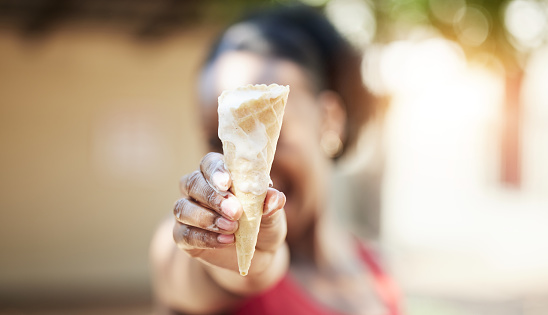 Black girl, hand and ice cream in outdoor in closeup for snack in summer or vacation with blurred in background. Dessert, melting and cone on holiday with person holding, tasty, fresh and sweet food.